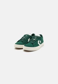 Adidași din suede verde cu accente albe, vârf rotund, talpă plată din cauciuc și design cu șireturi. Prezintă un logo în formă de stea pe lateral.