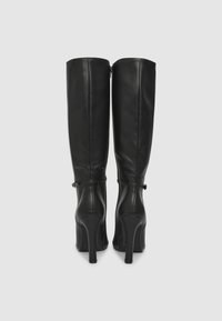 Stivali neri in pelle a stiletto al ginocchio con una texture liscia, chiusura con zip sul retro e dettagli con cinturino alla caviglia. Tacchi cilindrici alti.