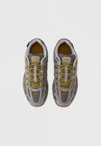 „Nike“ sportbačiai su pilkos spalvos tinklelio viršumi, geltonais raišteliais ir oranžiniais akcentais. Dizainas apima paminkštintą apykaklę ir tekstūruotą pado dalį, užtikrinančią sukibimą.