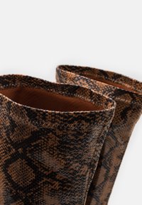 Braune Schlangenprint-Stiefel mit einer strukturierten Oberfläche, die eine schlanke Form aufweisen und kontrastierende schwarze Nähte entlang der Öffnung haben.