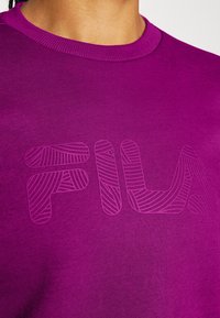 Koszulka z logo FILA w jasnopurpurowym kolorze, wykonana z bawełny, z teksturowanym, wytłoczonym logo z wzorzystym wzorem. Okrągły dekolt, krótkie rękawy.