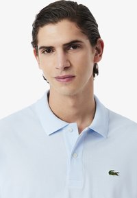 Polo shirt azzurro chiaro realizzato in morbido cotone, con una chiusura a tre bottoni e un logo di coccodrillo ricamato sul lato sinistro del petto.