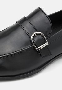 Mustad nahast loaferid sileda pinnaga, hõbedase kinnituse ja äärte ääres õmblustega.