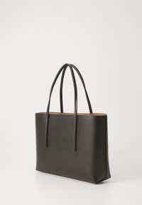 Svart lær tote-veske med to lange håndtak, satt mot en enkel hvit bakgrunn, som viser dens stilige og minimalistiske design.