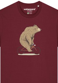 T-shirt bordeaux avec un graphique d'un ours faisant du vélo rouge. Le design est simple et illustré dans des tons neutres.
