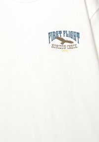 Weißes Baumwoll-T-Shirt mit einem Druckdesign, das "FIRST FLIGHT", eine Adlergrafik und "HORIZON CHECK 1991" in Blau, Braun und Gelb zeigt.