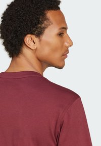 Burgundska bombažna majica s krožnim izrezom, kratkimi rokavi in gladko teksturo, s prijateljskim posnetkom hrbtne strani in ramen.