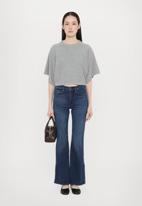 Top grigio corto, jeans scuri a zampa d'elefante, ballerine nere e una piccola borsa marrone; tessuto liscio, vestibilità rilassata, dettagli di design discreti.