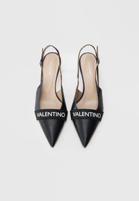 Mustat nahkaiset slingback-kengät, joissa on terävät kärjet ja leveä musta hihna, jossa lukee "VALENTINO" valkoisilla kirjaimilla edessä.