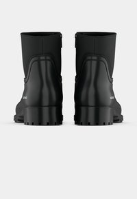 Botas de borracha pretas até ao tornozelo com uma sola texturizada, acabamento suave e fecho éclair na parte de trás, apresentando um design elevado nas laterais e um logotipo.