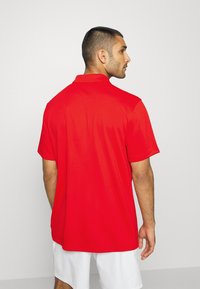 Rød polo skjorte med krave og korte ærmer, der har en glat tekstur og en løs pasform. Bagsiden viser ingen synlige mønstre eller detaljer.