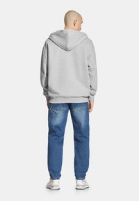 Szara bluza z kapturem o luźnym kroju, zestawiona z jasnoniebieskimi dżinsami. Widziane szwy i ściągacze, noszona z białymi sneakersami.