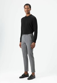 Zwart gebreide trui, getailleerd, grijze op maat gemaakte broek met zijzakken, platte voorkant, smalle pijpen; afgewerkt met zwarte loafers.