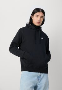 Mustahdina musta huppari, jonka hihnat ovat säädettävissä, edessä tasku ja valkoinen Nike-logo rinnassa. Yhdistetty vaaleansinisiin farkkuihin.