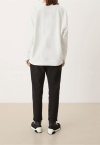 Felpa bianca con vestibilità rilassata, polsini e orlo a costine, abbinata a pantaloni della tuta neri. Le sneakers presentano una parte superiore nera e una suola bianca.