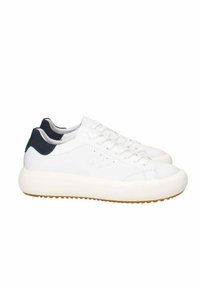 Sneakers bianchi in pelle con punta rotonda, superficie testurizzata e dettagli blu navy sul tallone. Suola in gomma spessa di colore chiaro.