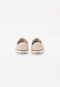 Beežist kanvasest madalad tennisetossud mustade triipudega ja valgete kummitaldadega, millel on "CONVERSE ALL STAR" bränding kannal.
