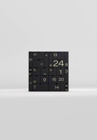 Black advent calendar with gold numbers on square compartments, featuring a matte texture and smooth edges. Contains 24 drawers for items.