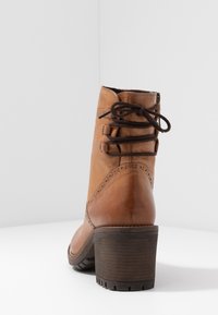 Hnědá kožená kotníková bota s texturovaným povrchem, zaoblenou špičkou, dekorativním šitím a vrstveným podpatkem. Obsahuje krajkové prvky na zadní straně.