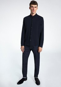 Camisa de botones color marino con cuello puntiagudo, tela suave y mangas largas, combinada con pantalones de mezclilla oscuros y zapatos negros.