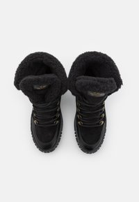 Botas negras con un exterior de ante y cuero, que cuentan con un forro de felpa texturizada y hardware metálico en tono dorado para los cordones.