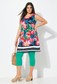 Kwiatowa tunika na czarnym tle, z dużymi różowymi i zielonym wzorami; zestawiona z turkusowymi legginsami i beżowymi sandałami na koturnie. Pleciona torba jako dodatek.