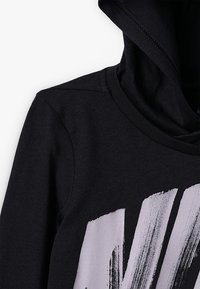 Mustaphoodie, jossa on pehmeä rakenne, etupuolella iso valkoinen siveltimenveto- grafiikka ja rento kauluksen muotoilu.