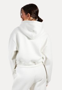 Witte oversized hoodie met een grote capuchon, ribbelzoom en zacht katoenmateriaal. Kenmerken zijn verlaagde schouders en een ontspannen pasvorm.