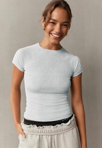 Lys grå tætsiddende ribbet t-shirt med korte ærmer, rund hals og let struktureret stof, parret med lys grå bukser med afslappet talje.
