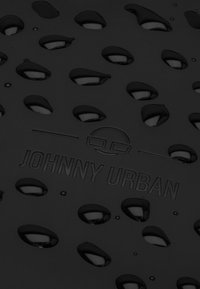 Fekete gumi szőnyeg ovális kivágásokkal, texturált felülettel és dombornyomott „JOHNNY URBAN” logóval, sima felületű és változó mélységgel.