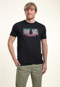 Camiseta de algodón negra con un colorido estampado gráfico de diseño retro, que muestra figuras y texto en la parte frontal.