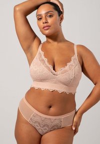 Nude kanten bralette met geschulpte randen en verstelbare bandjes, gecombineerd met bijpassende kanten en doorschijnende hipster slipjes, beide met ingewikkelde patronen.