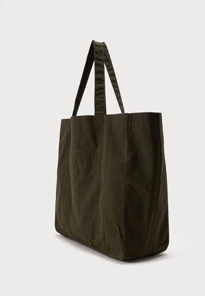 Grand sac fourre-tout en tissu vert foncé avec deux longues poignées et une base rectangulaire, debout sur un fond clair.