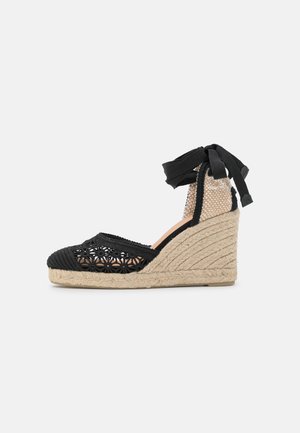 Sandale compensée noire en espadrille avec talon en jute tressé, motif floral découpé sur l'avant-pied et liens noirs à nouer autour de la cheville.