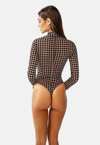 Dlouhý rukáv body s houndstooth vzorem, s vysokým límečkem, průhledným materiálem a odvážným vykrojením, převážně v černé a béžové barvě.