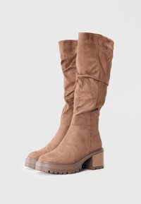 Botine din suede maro, până la genunchi, cu un design căzut, talpă din cauciuc masiv și toc stratificat. Accente texturate pe toc.