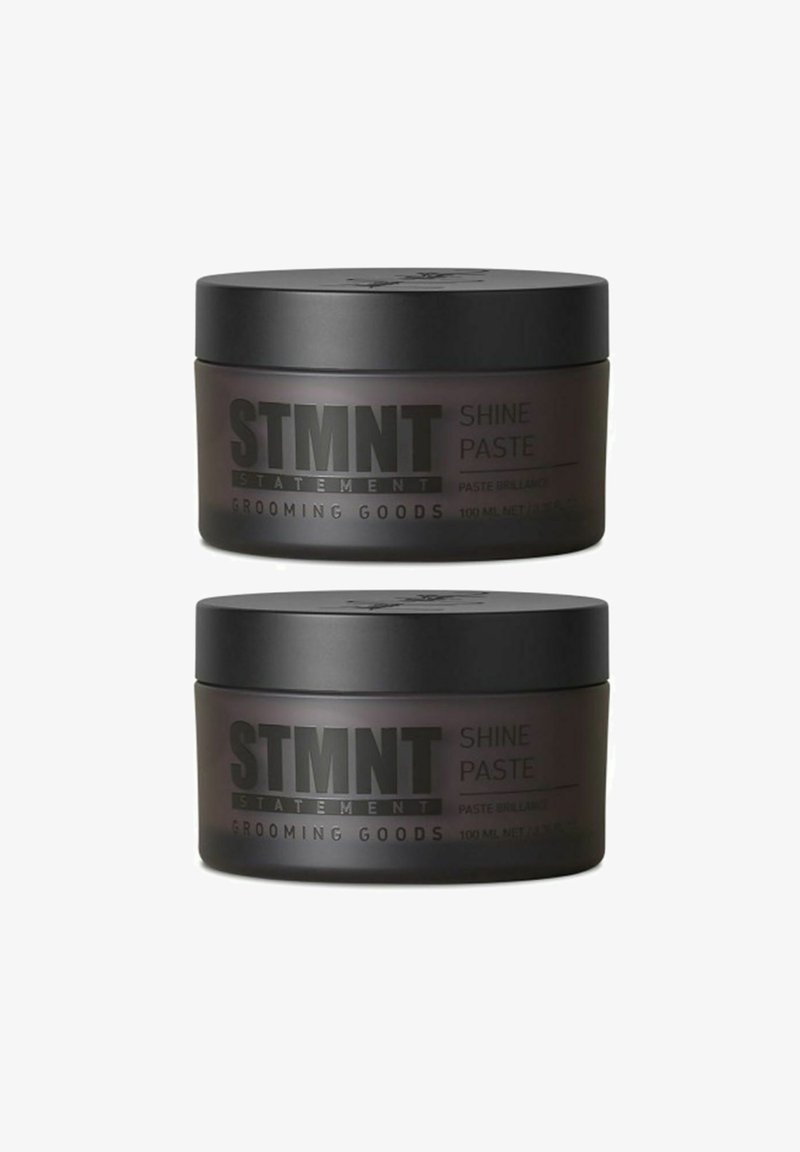 Zwei Gläser STMTNT Shine Paste, matte schwarze Deckel, transparente dunkle Behälter, gekennzeichnet mit fetter weißer Schrift, 100 ml.