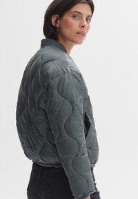 Gequilted, donkergrijze bomberjack met een geribde kraag, twee zijzakken en een gestructureerd oppervlaktepatroon.