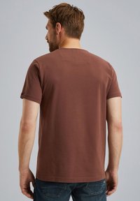 Braunes Baumwoll-T-Shirt mit kurzen Ärmeln, Rundhalsausschnitt und einer kleinen Nahtdetails auf der Rückseite, kombiniert mit blauen Jeans.