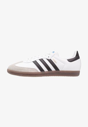 Biały sneaker Adidas Samba z czarnymi paskami, zamszowym noskiem, brązową podeszwą i złotym tekstem "SAMBA" z boku.