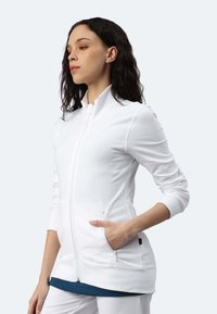 Giacca bianca con zip, colletto alto, maniche lunghe e due tasche frontali. Presenta una texture liscia e polsini a coste.
