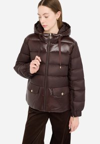 Giubbotto puffer marrone con finitura lucida, cappuccio, chiusura con zip frontale e due tasche anteriori con dettagli dorati. Polsini a coste e cordino regolabile.