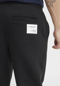 Zwarte katoenen sweatpants met een achterzak en een rechthoekig label met de tekst "11 PROJECT". Soepele textuur en elastische tailleband.