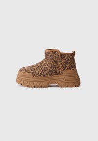 Botín de plataforma con parte superior de estampado de leopardo marrón y negro y suela gruesa color beige sobre fondo blanco.