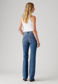 Jean flared taille haute en denim bleu avec une texture délavée, doté d'une étiquette en cuir beige et de poches arrière brodées.