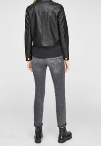 Chaqueta de cuero sintético negra recortada sobre una blusa negra, combinada con jeans grises y botas negras hasta el tobillo, vista desde atrás.