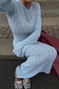 Helehall sinine kudumised särk ja sobiv pikk seelik, mis on valmistatud avatud kudumiga kangast, koos must-valgete triibuliste lapikute kingadega. Taustal punane kott.