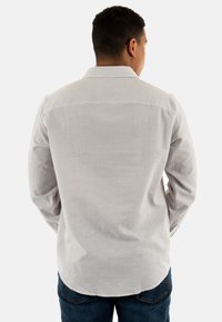 Camicia a maniche lunghe di colore grigio chiaro con un design a coste testurizzato. Presenta un colletto a punta e un orlo curvo. Indossata con jeans blu.