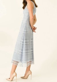 Světle modré krajkové šaty se střední délkou, s propracovanými vzory a výřezy. Nosí se s tělovými lodičkami.