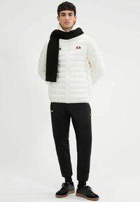 Chaqueta blanca acolchada con una bufanda negra, pantalones negros y zapatos negros. Presenta acentos de logo y un diseño ajustado. Estilo minimalista.